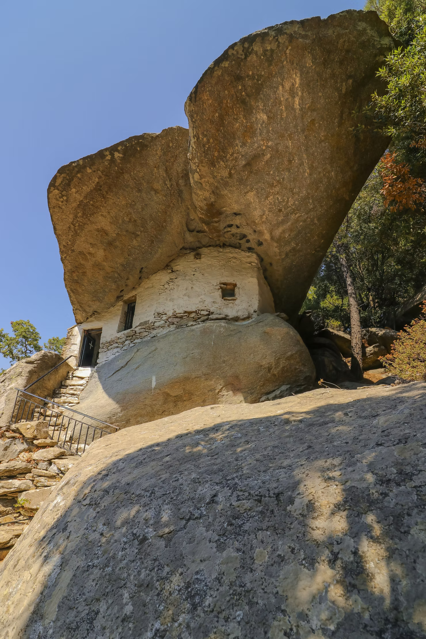 Ancient stone pirate house built beneath a massive rock in Ikaria